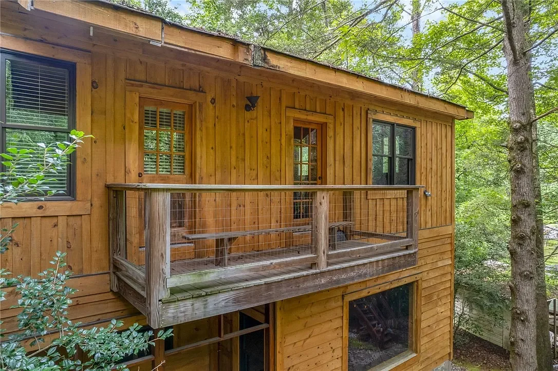 Wooden house with a small balcony, surrounded by trees with green leaves.