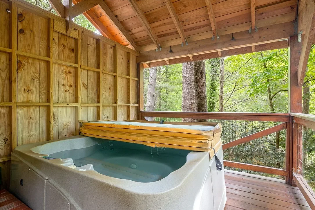 A hot tub on a wooden balcony surrounded by trees, with a wooden roof overhead and wood-paneled walls.