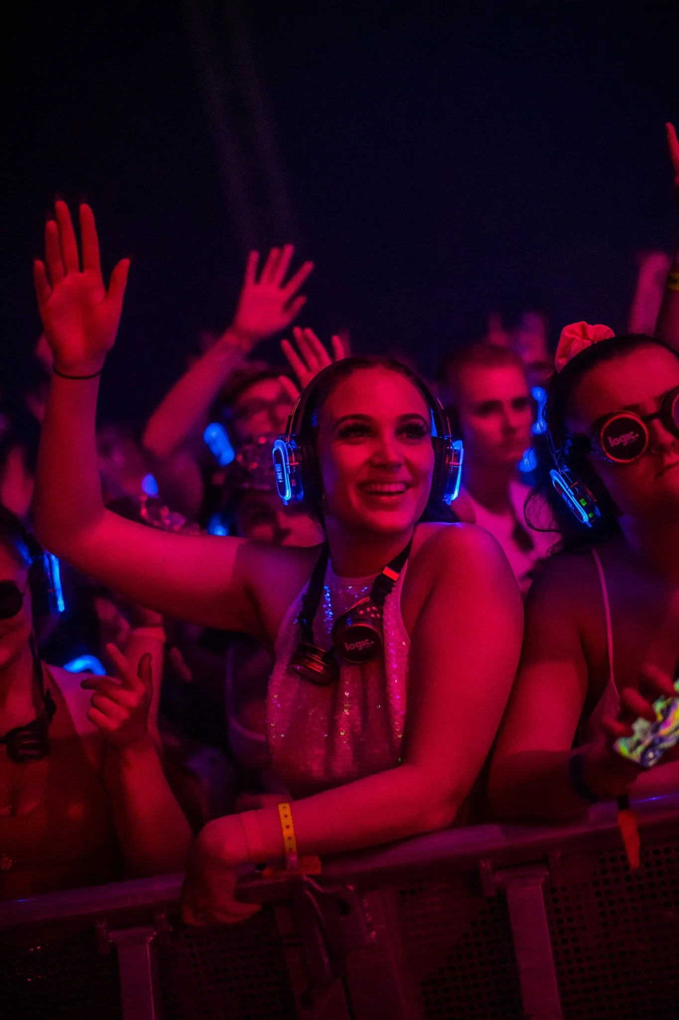 People at a concert or nightclub wearing headphones and enjoying the event, illuminated by pink and purple lights.