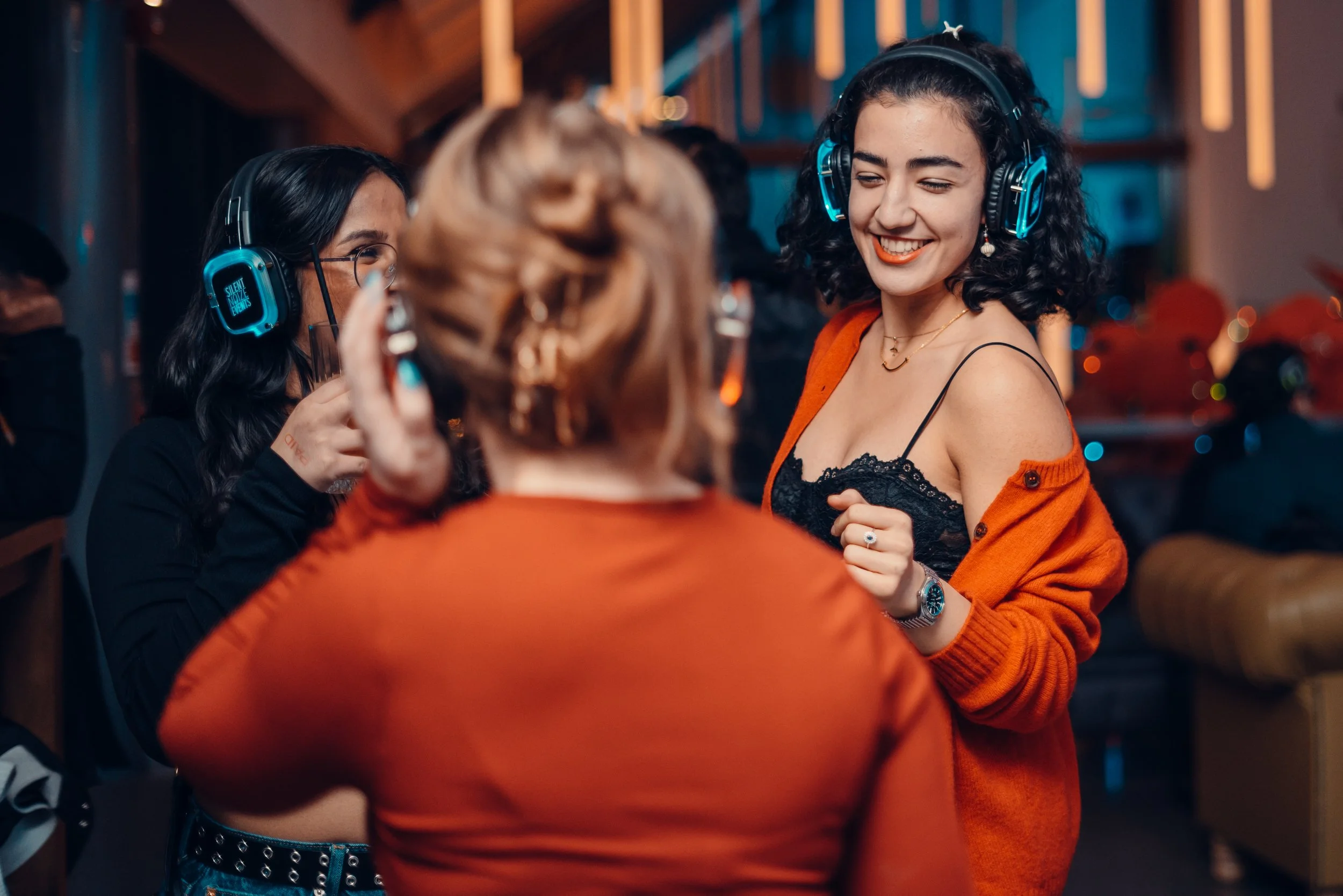 Group of people enjoying music with headphones at a lively indoor party, smiling and dancing.