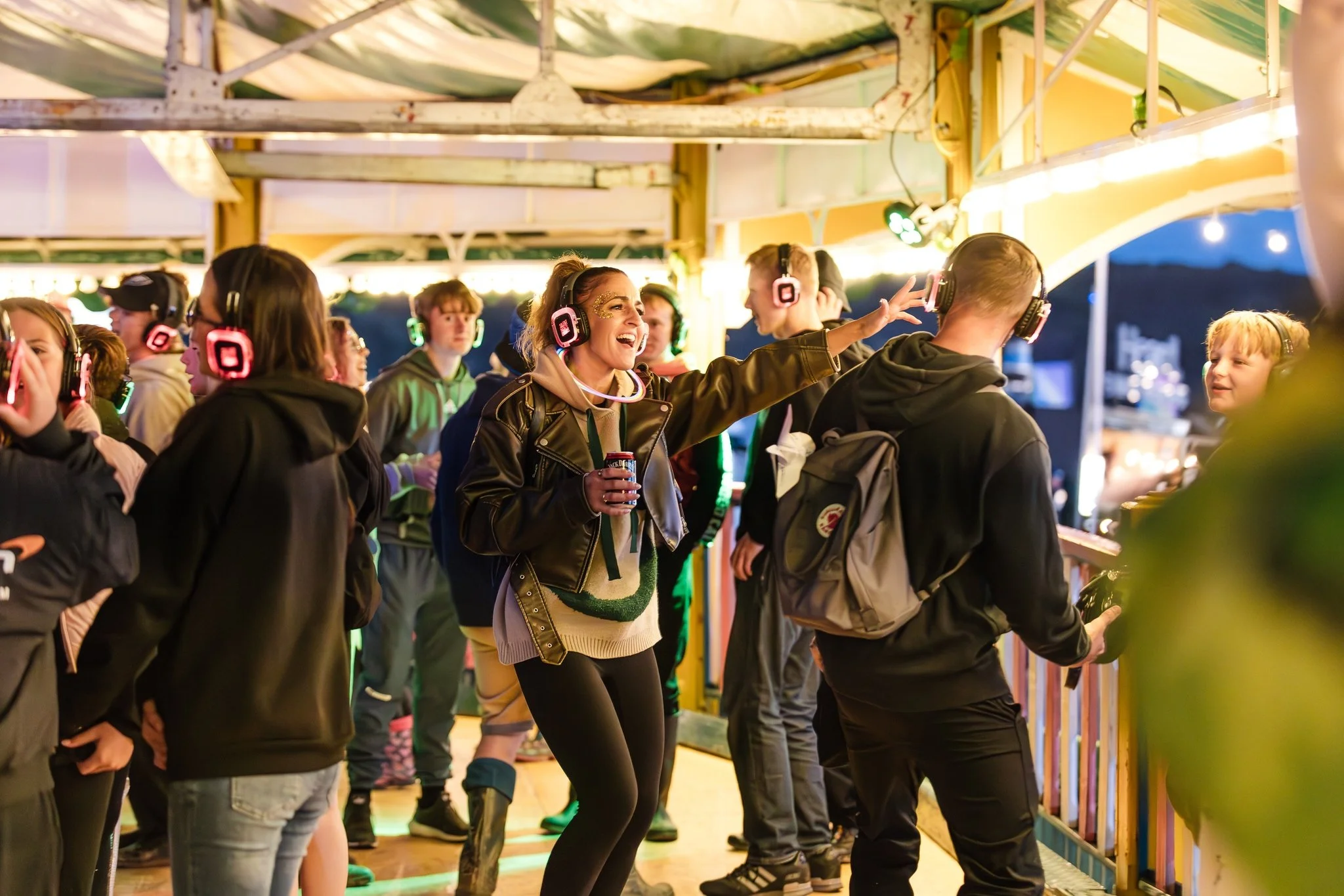 Group of people enjoying a carnival ride, wearing headphones and having fun, with bright colorful lights.