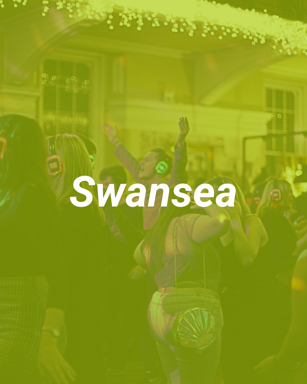 People dancing and enjoying music at a lively indoor event with colorful lights and a festive atmosphere, representing Swansea.