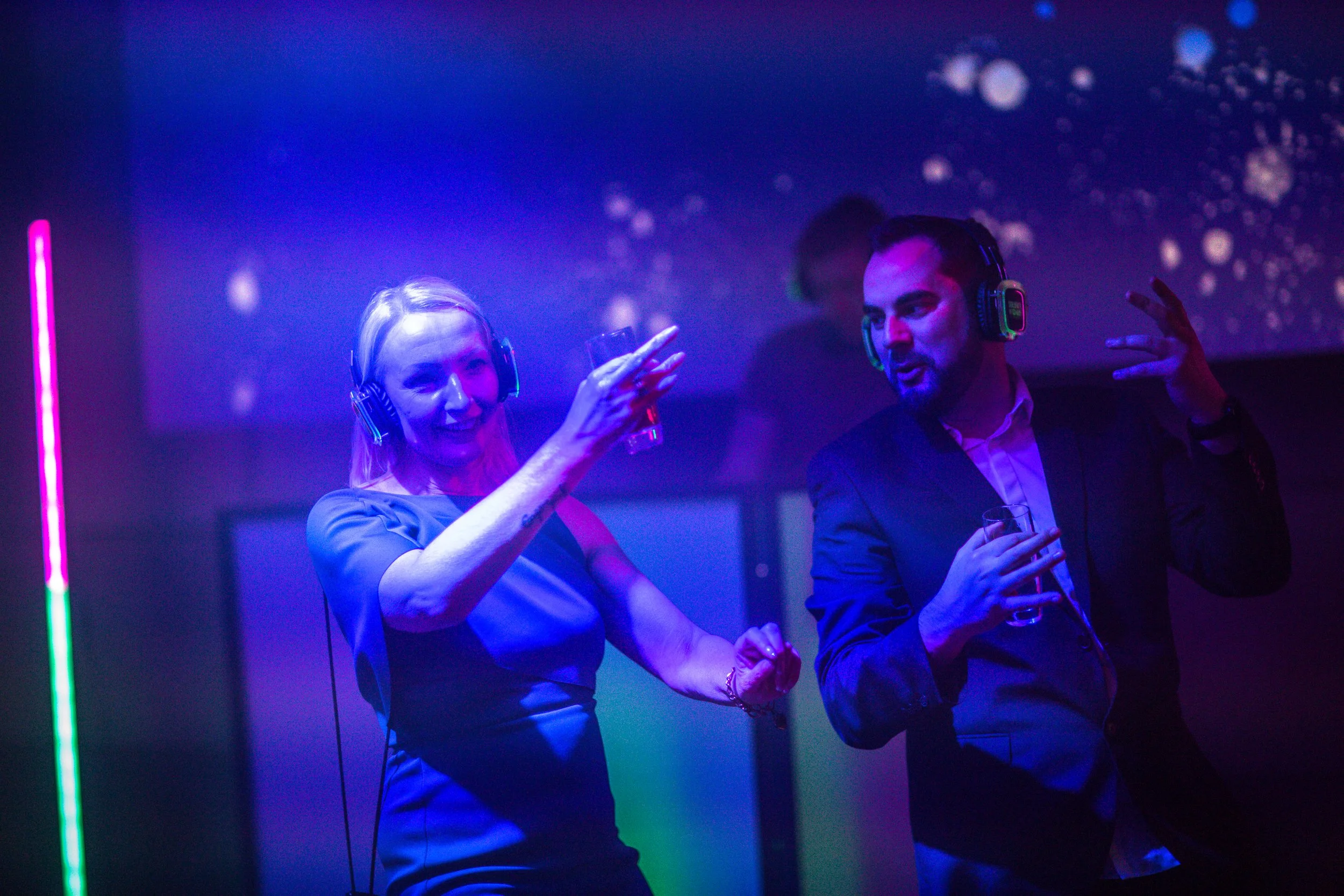 Two people, a woman and a man, dancing and enjoying music at a nightclub, wearing headphones, with colorful lighting and a starry background.