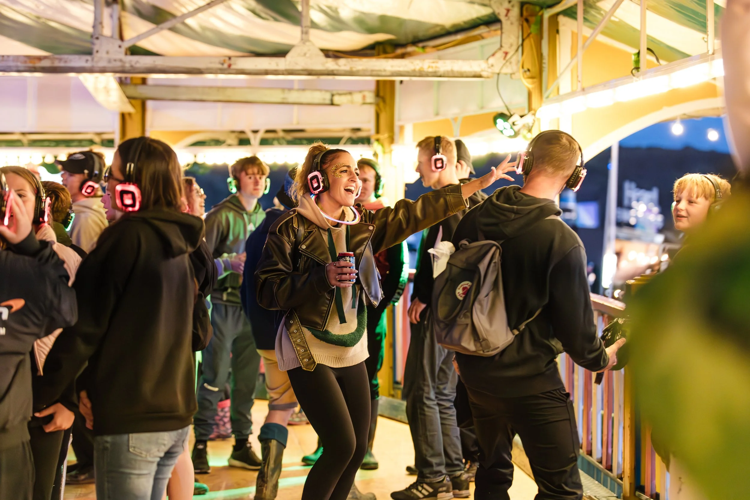 People wearing headphones dancing and enjoying music at an outdoor fair or festival during evening.