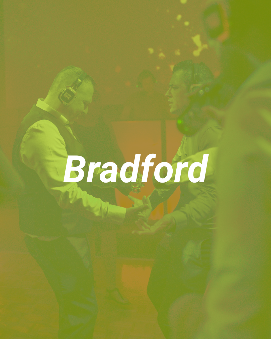 Two men shaking hands in Bradford, both wearing headphones, with colorful lights in the background.