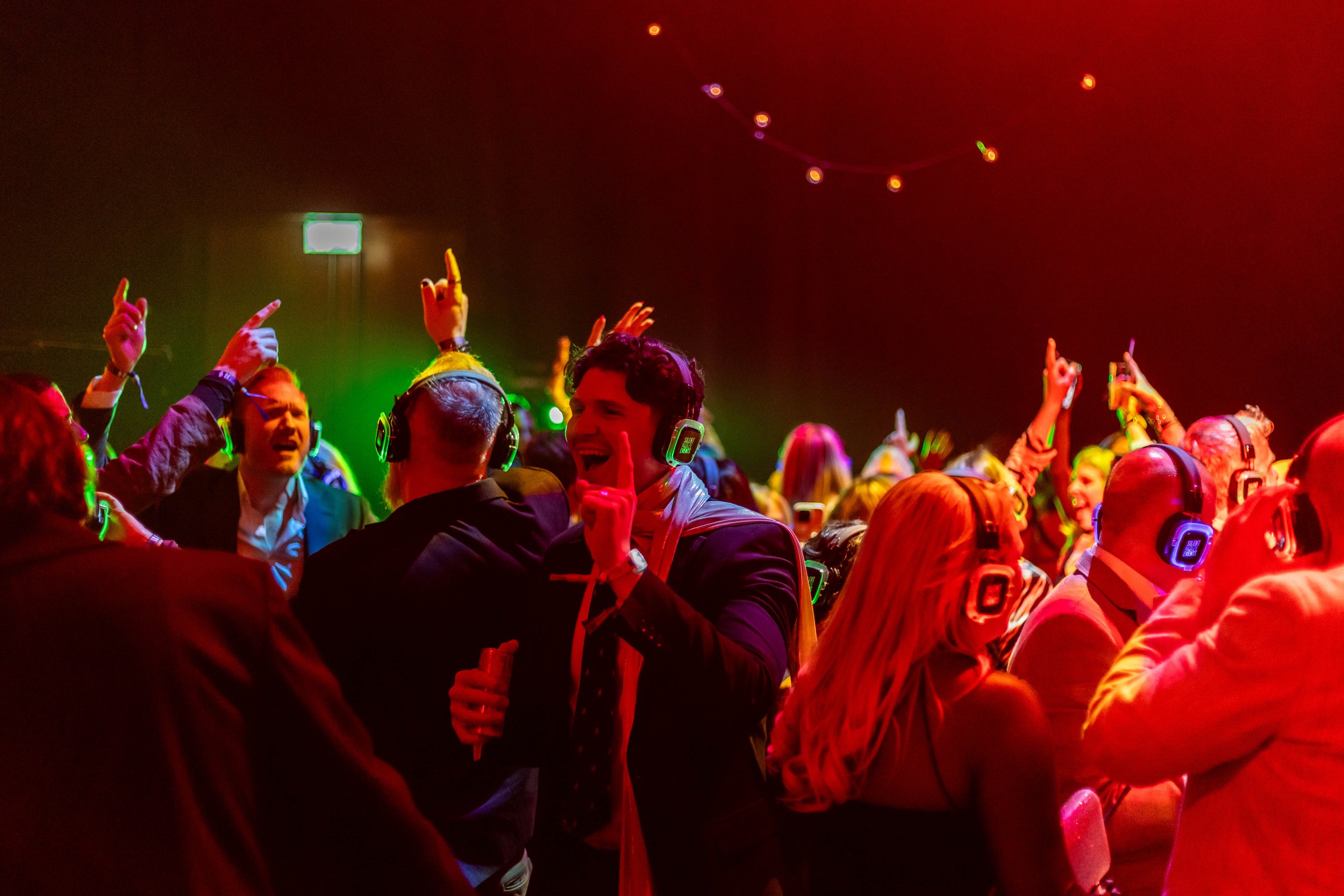 People at a party wearing headphones, dancing, and enjoying music in a colorful, lively setting.
