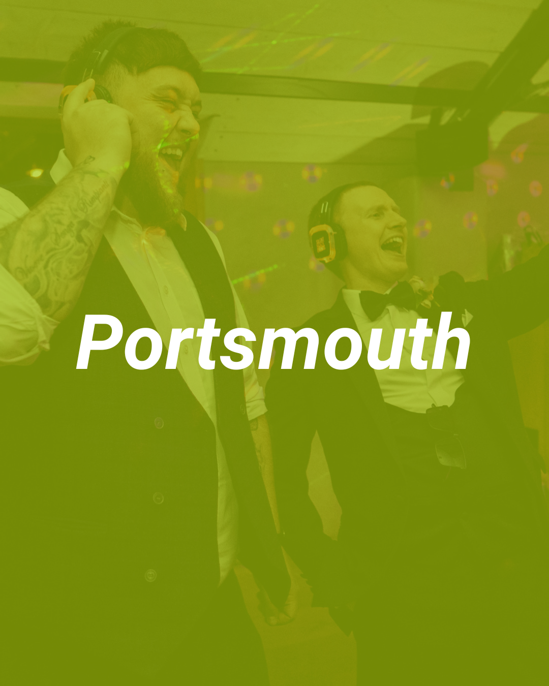 Two men dressed in tuxedos, one with tattoos and a beard, the other wearing headphones, are smiling and celebrating at an event in Portsmouth.