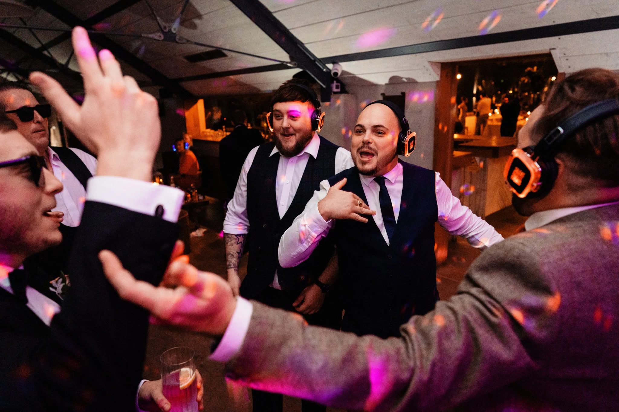People dancing and socializing at a party with colorful lights, some wearing headphones and formal attire.