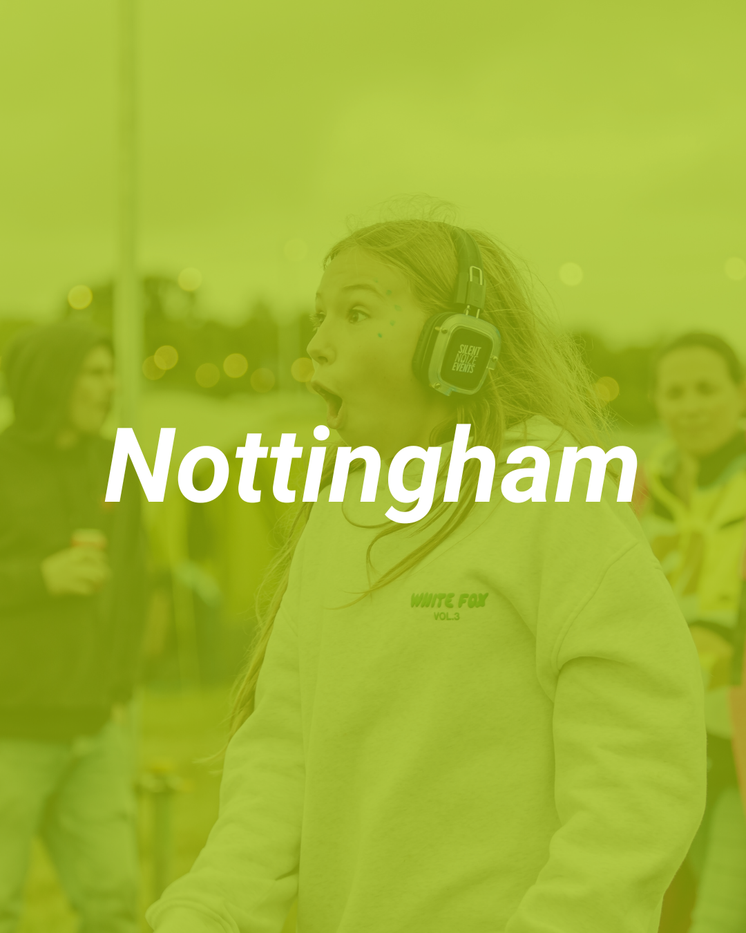 Young woman with surprised expression, wearing headphones, outdoors in Nottingham, with blurry people in the background.