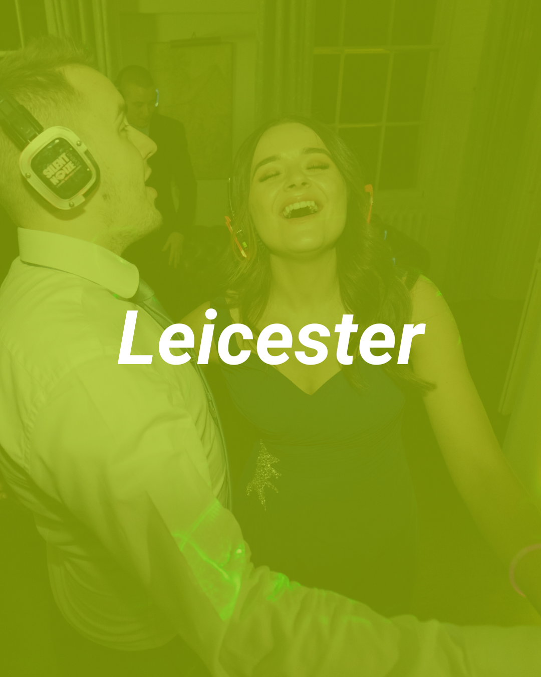 Group of people enjoying a celebration in a room, one woman singing with joy, a man wearing headphones smiling, festive atmosphere by Leicester.