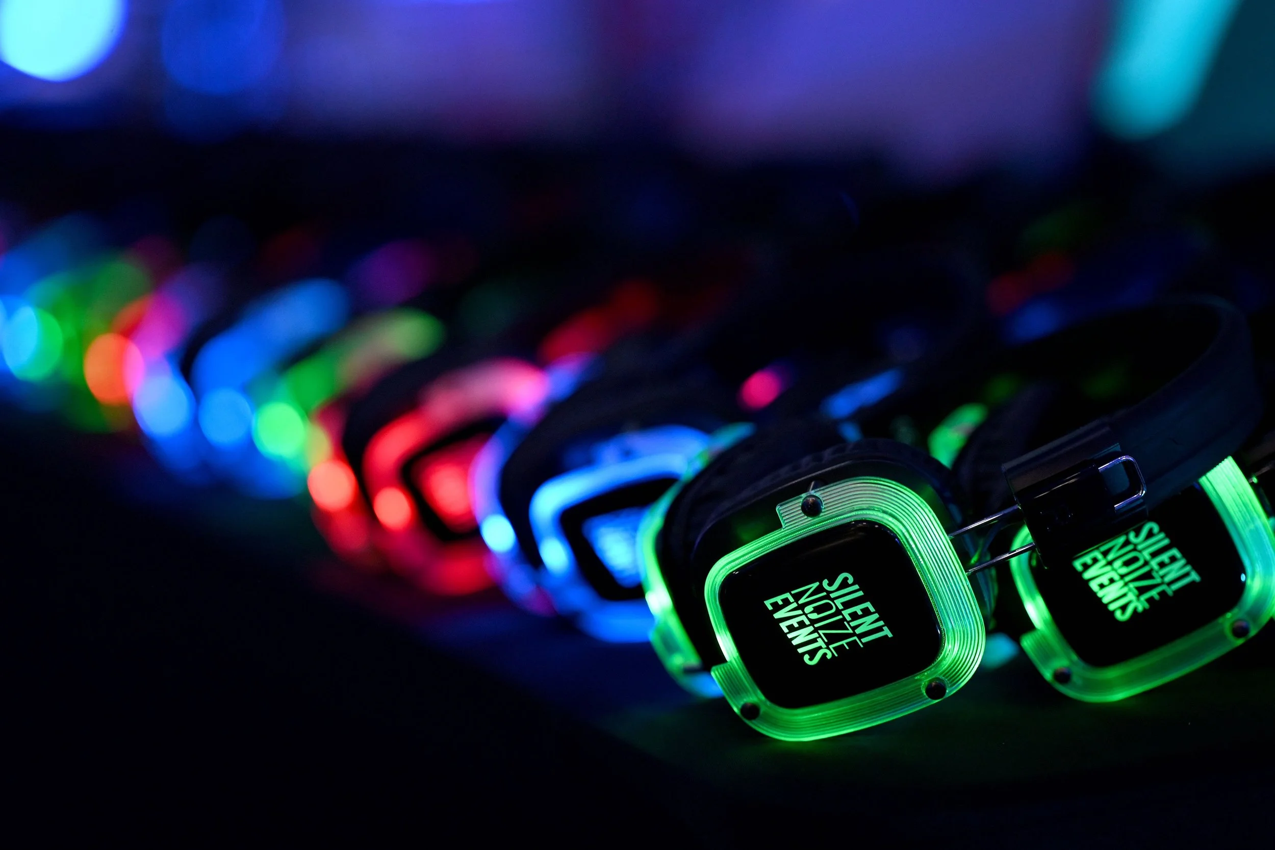 Multiple smartwatches with glowing green, blue, red, and purple lights, arranged in a diagonal line on a dark surface. The screen displays 'SILENT NOZZLE EVENTS' in green text.