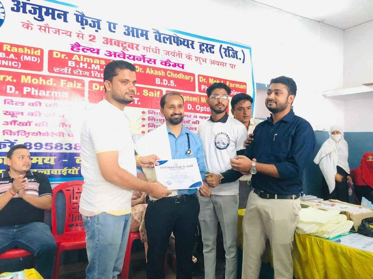 Group of men at a certificate awarding event, one man handing a certificate to another, with a colorful banner in the background.