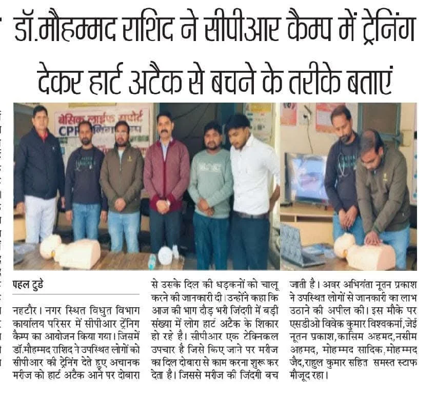 Group of men standing behind a table with what appears to be a training demonstration in a room, with a television and various posters on the wall. One man is working on a model of a human head.