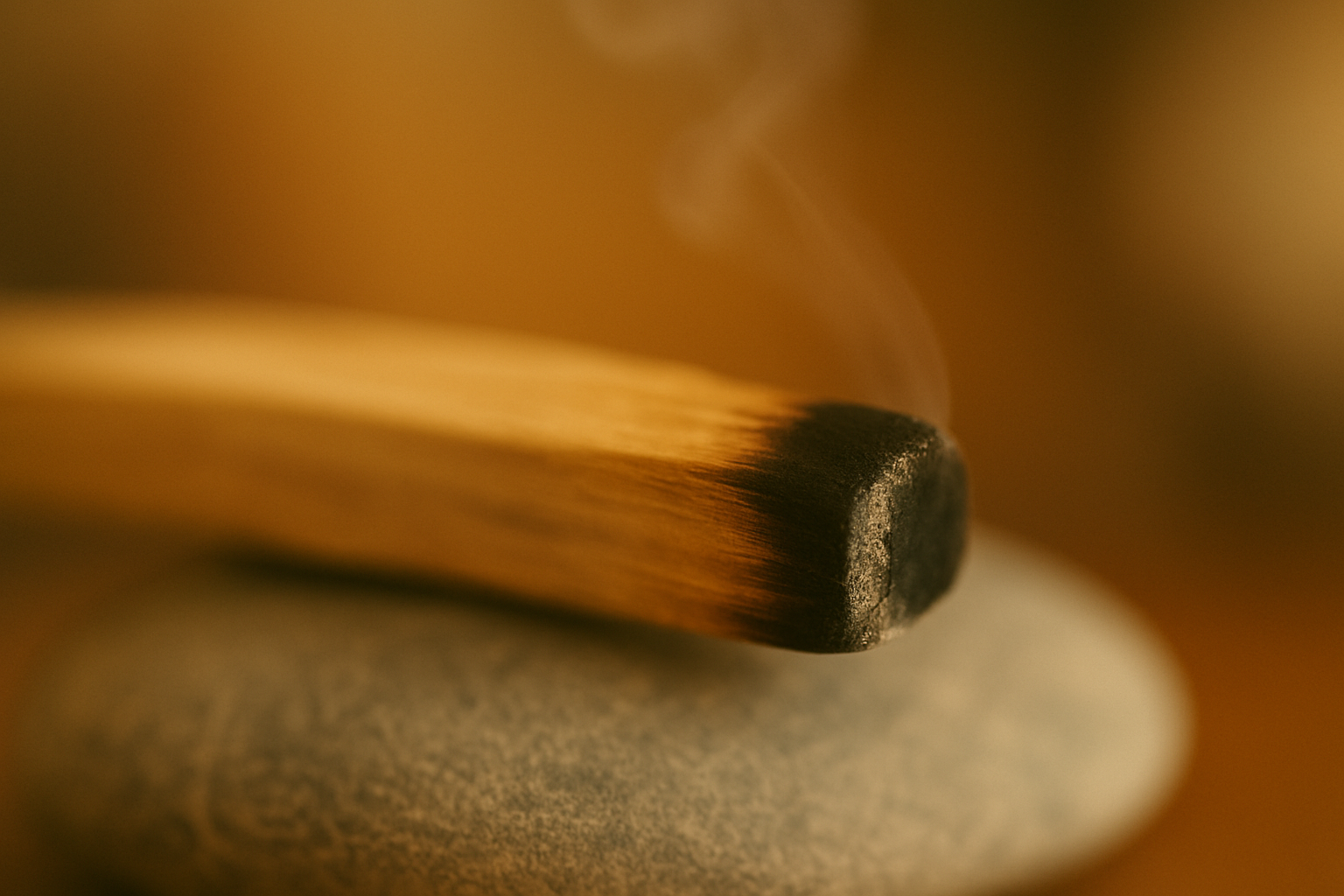 Close-up of a burning wooden matchstick resting on a stone surface, with smoke rising from the match head.