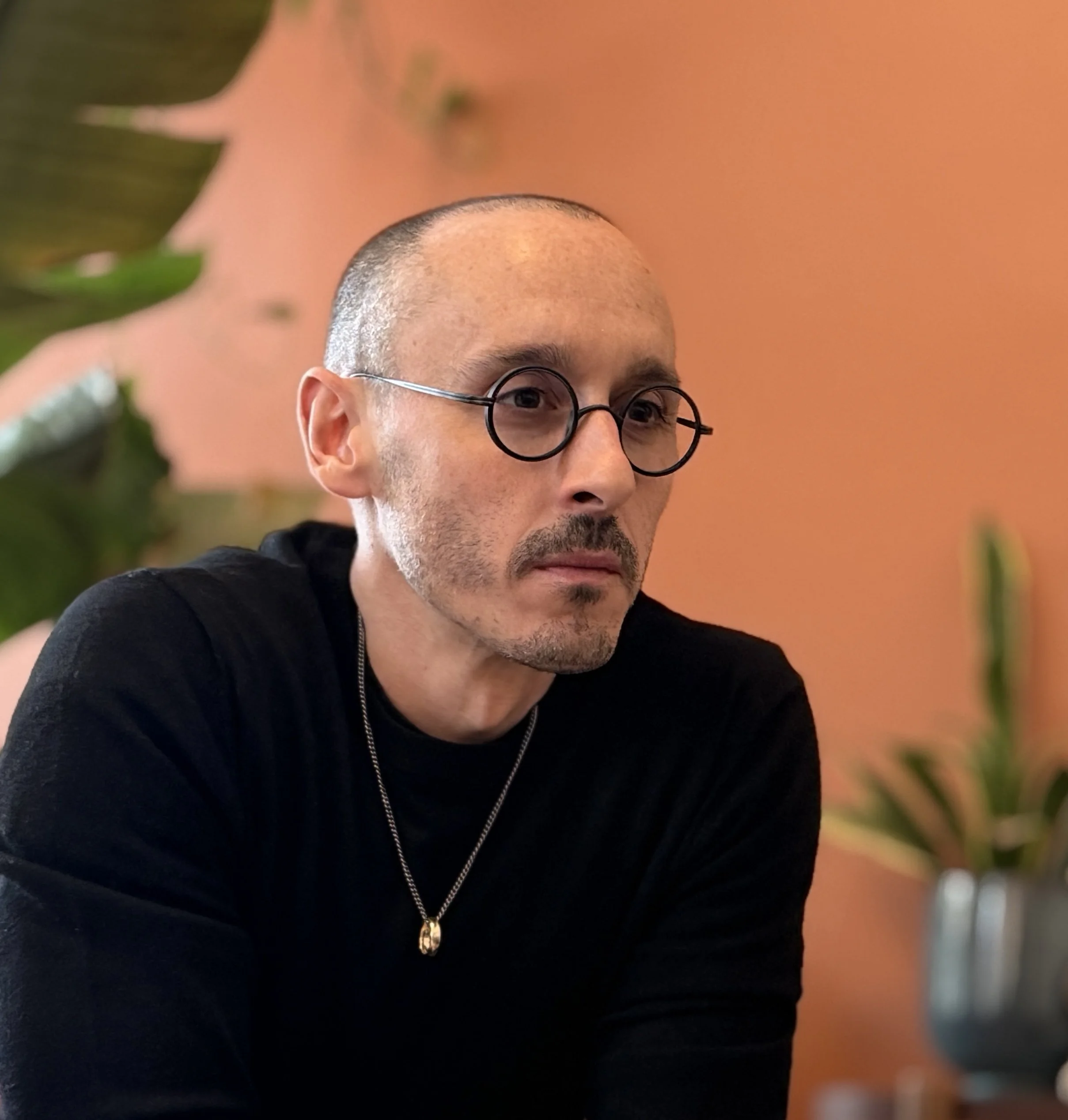 Portrait of Julien Lacaille wearing glasses and a black sweater against a warm orange background.