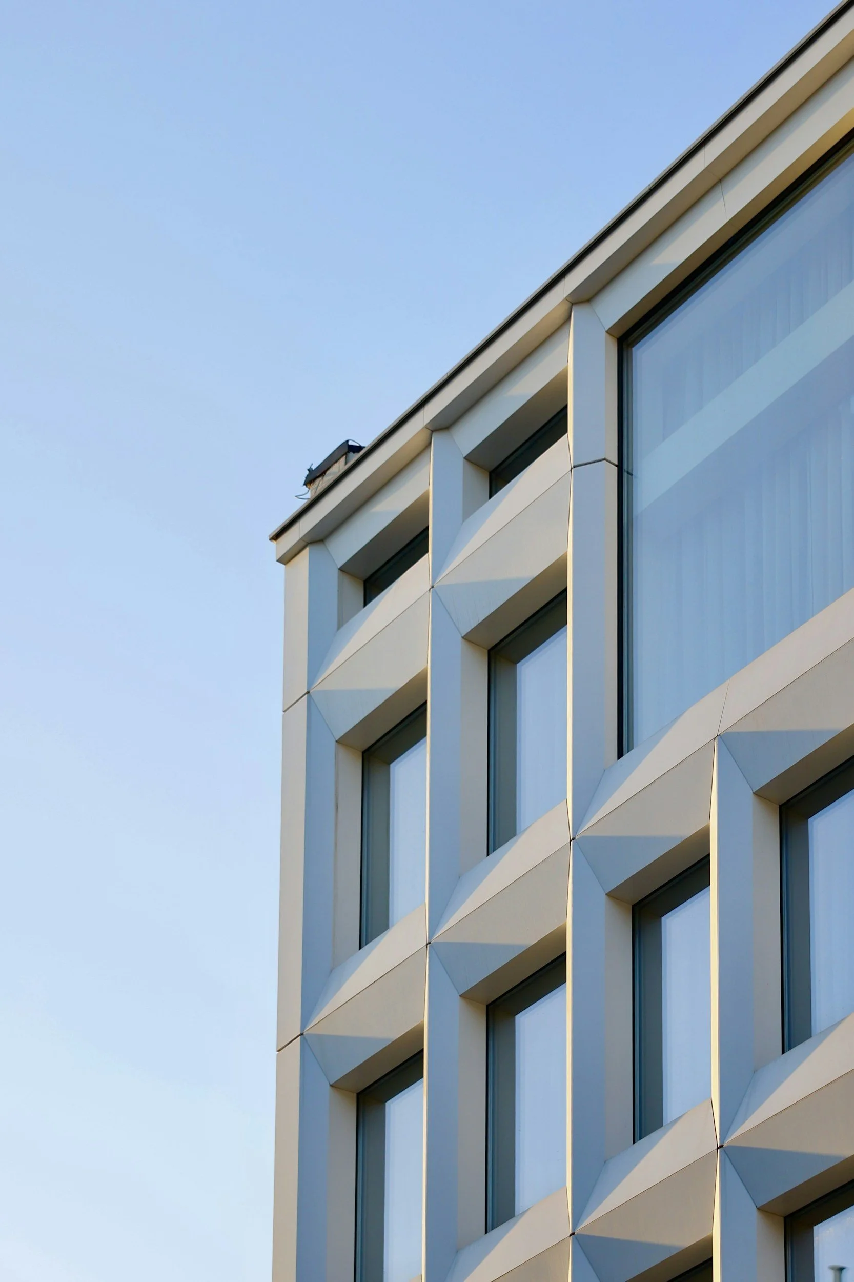 Close-up of a modern building's exterior with geometric window frames and a clear blue sky in the background.