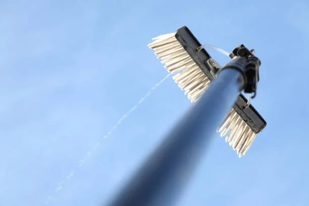 A street sweeper vehicle with rotating brushes cleaning the road surface from an upward angle against a clear blue sky.