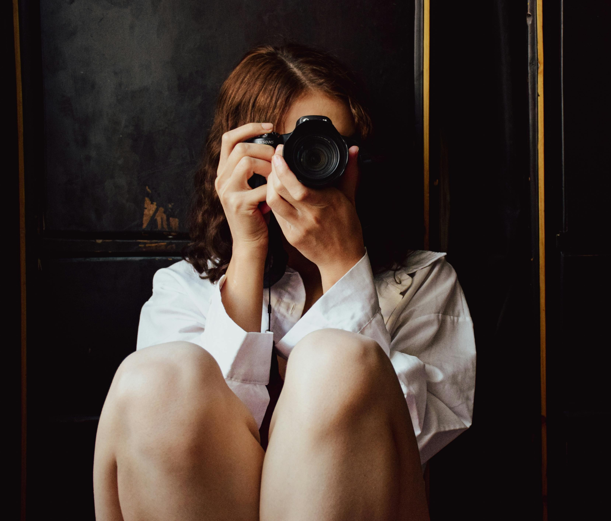 Photographer sitting cross-legged holding a camera up to their face