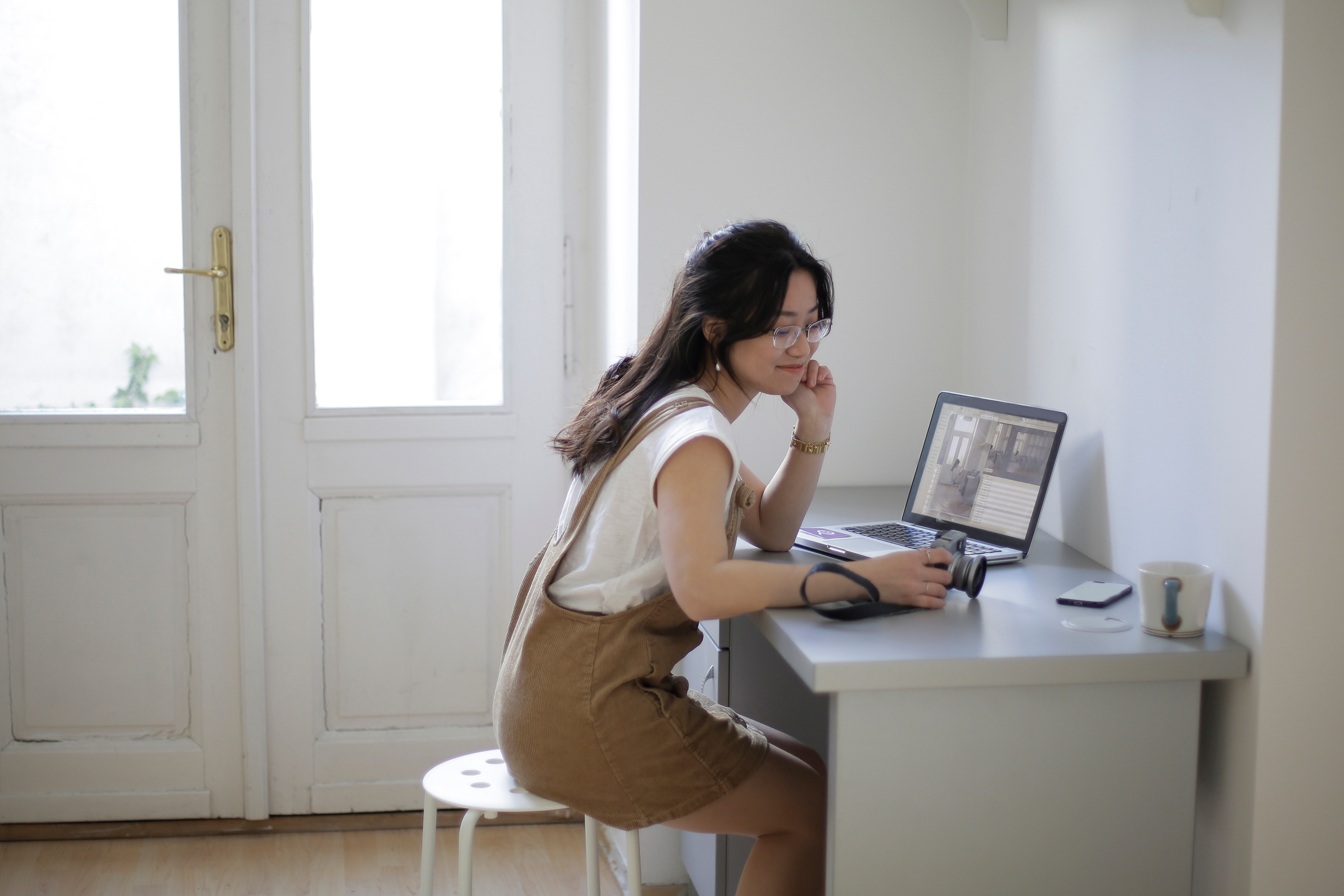Family Photographer sitting at a desk with a laptop, camera, smartphone, and mug working on her business.