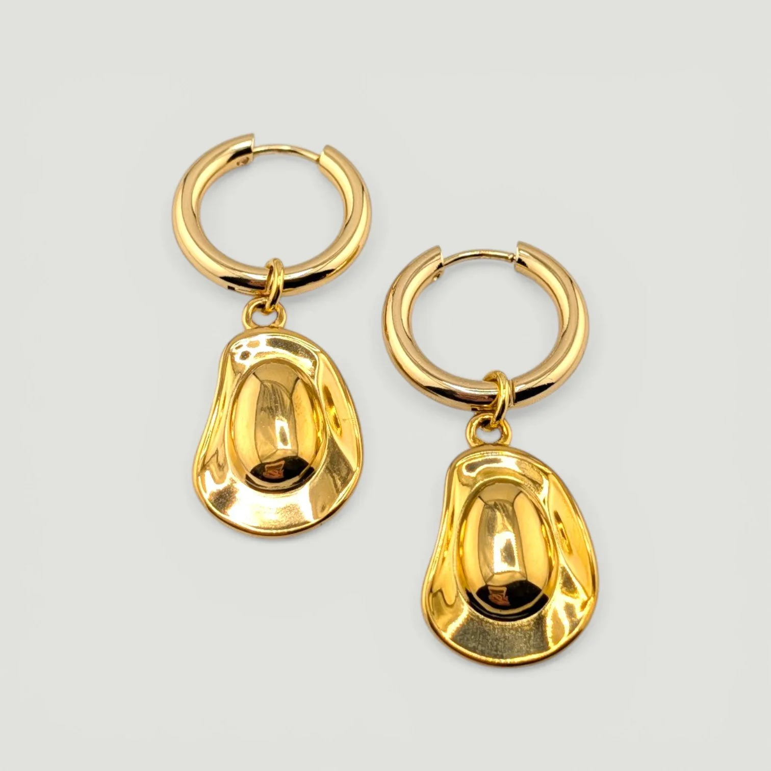 Gold cowboy hat charm huggie hoop earrings, stainless steel, flat lay