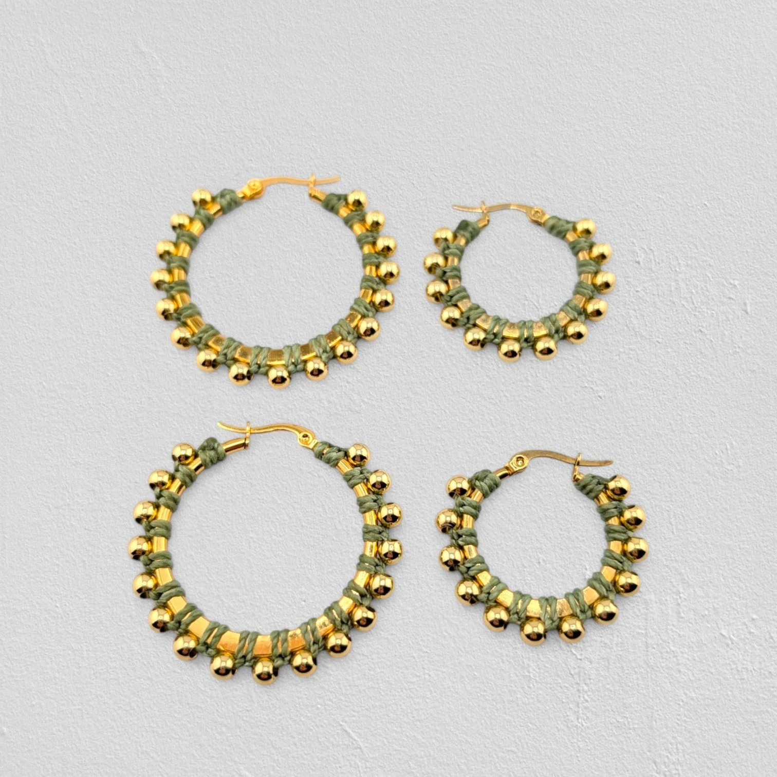 Light moss green beaded macramé stainless steel hoop earrings in gold, 30 mm and 40 mm sizes side by side, flat lay on a neutral background