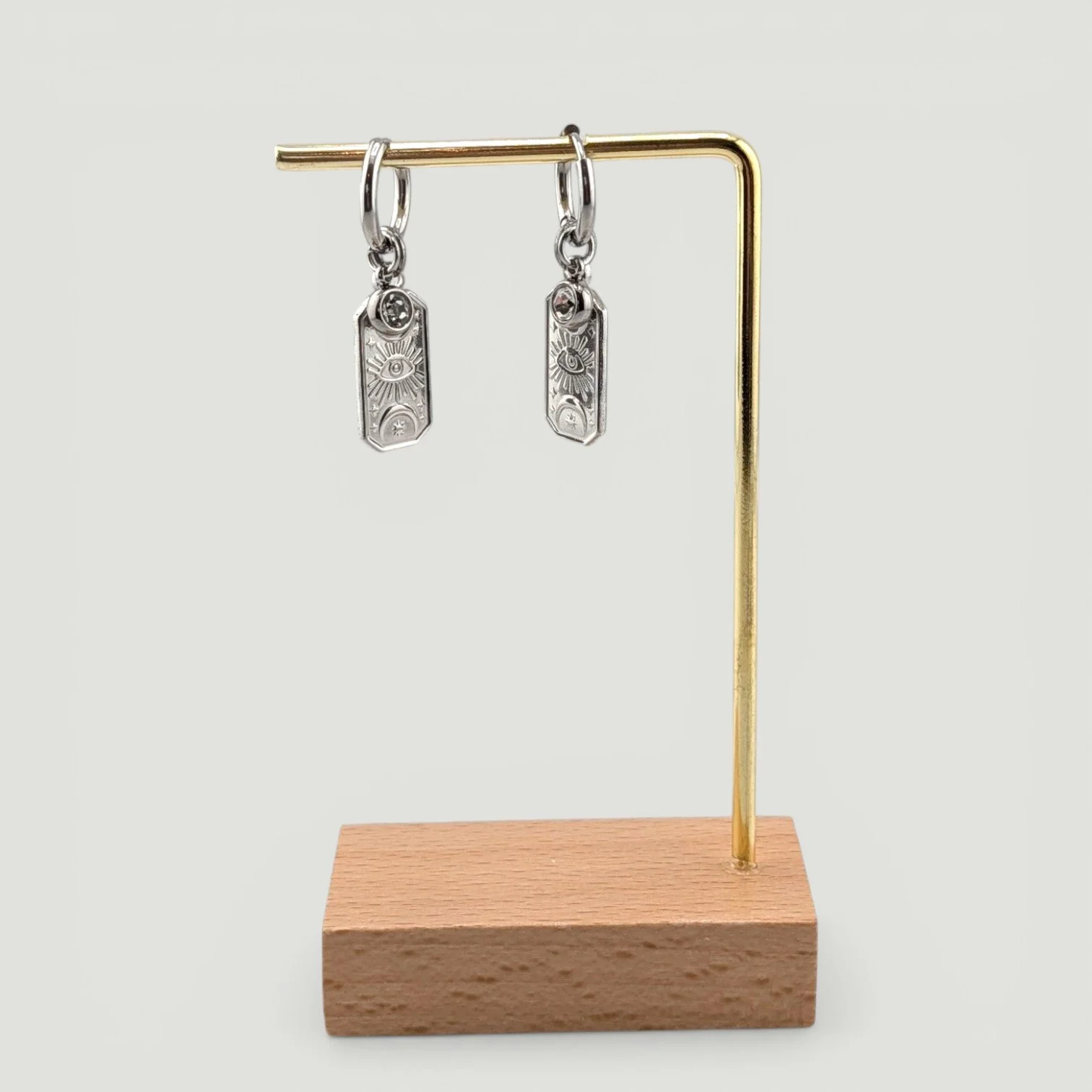 Gold evil eye stainless steel huggie hoop earrings with rhinestone and medallion charms on display