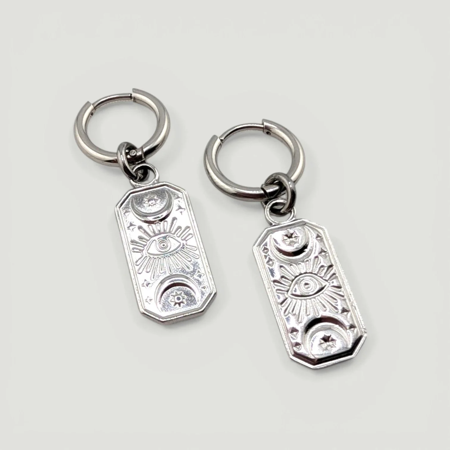 Gold stainless steel huggie hoop earrings with evil eye medallion charms flat lay