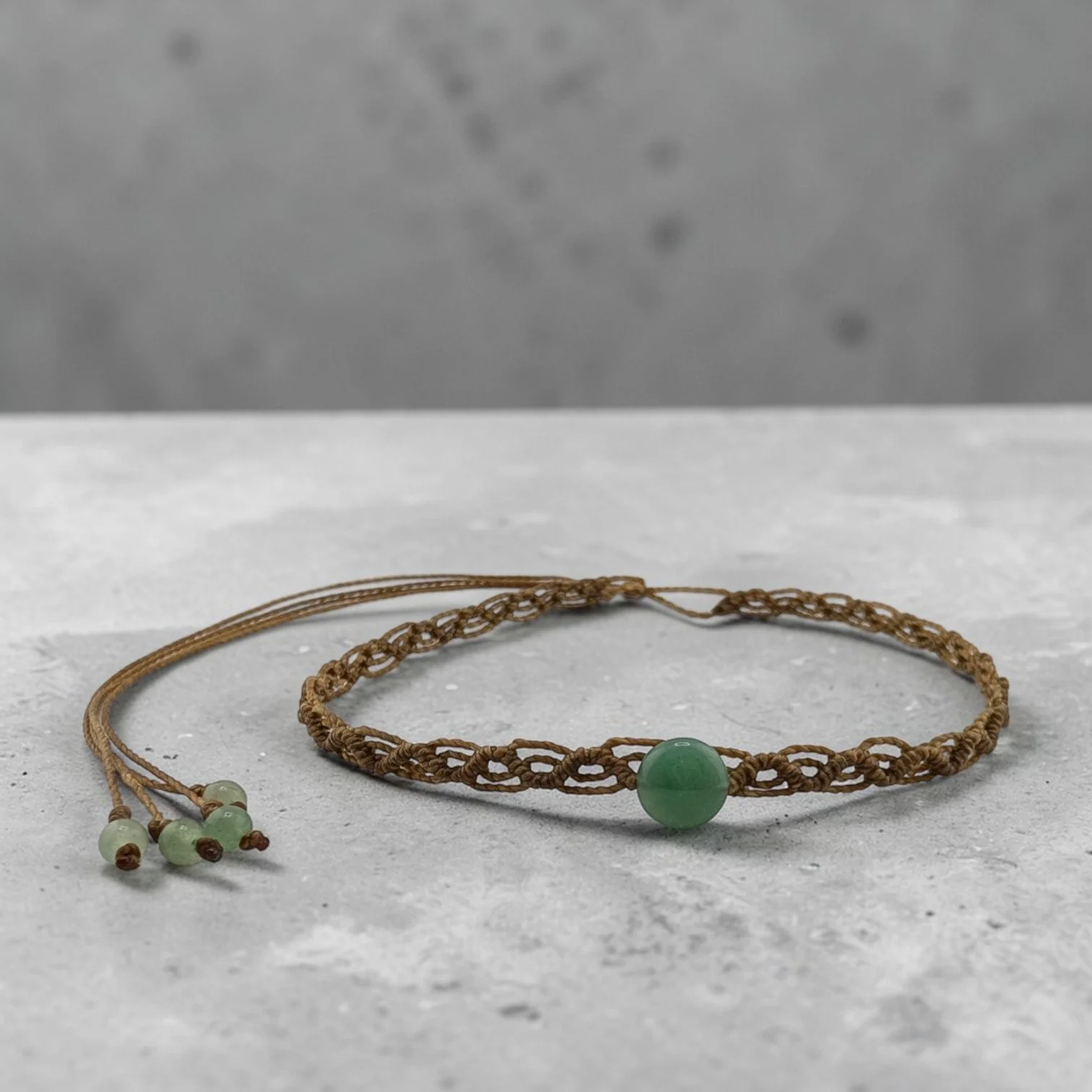 Western macrame woven choker with an aventurine centerpiece displayed on a textured ciment shelf