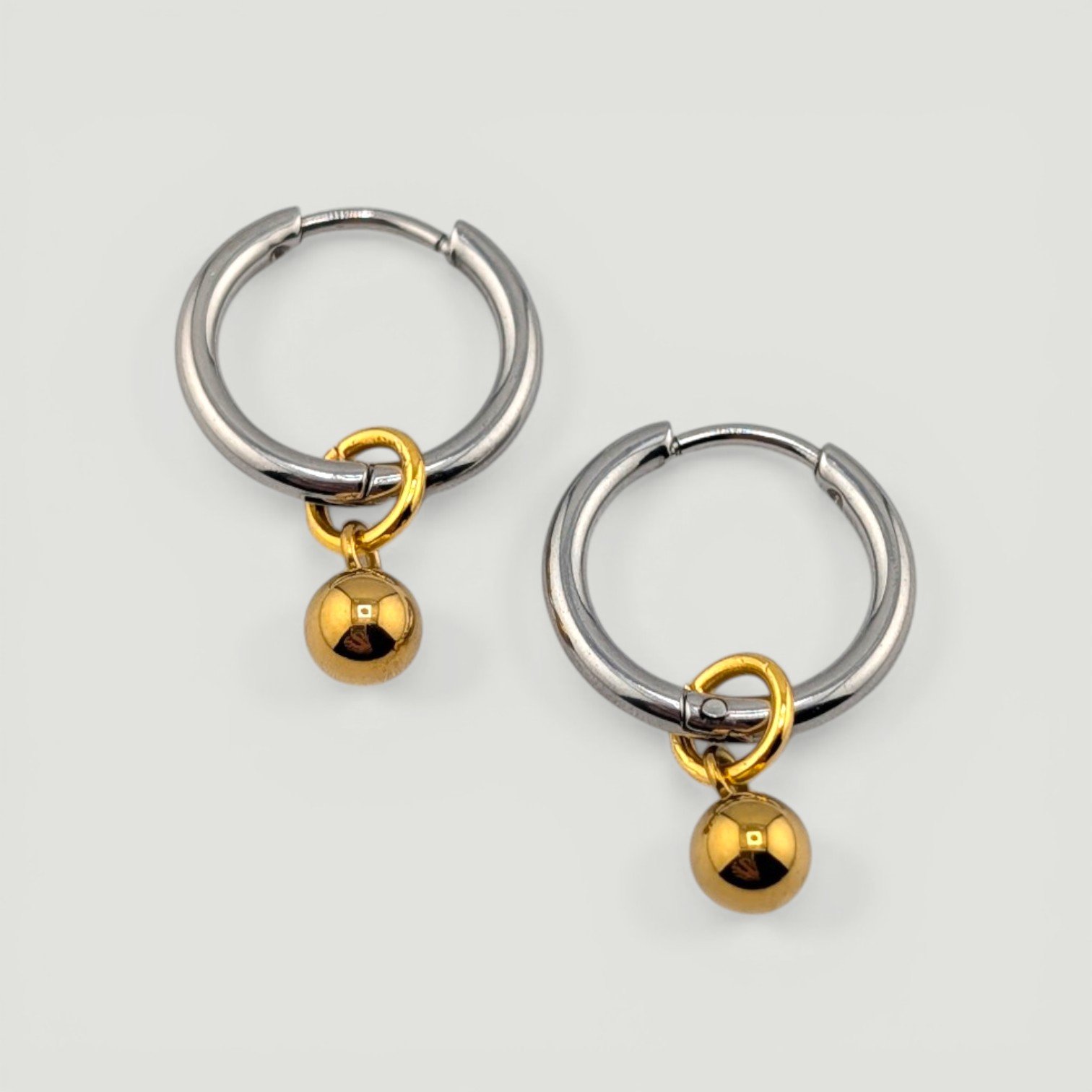 Silver stainless steel huggie hoop earrings with gold bead charm two-tone flat lay