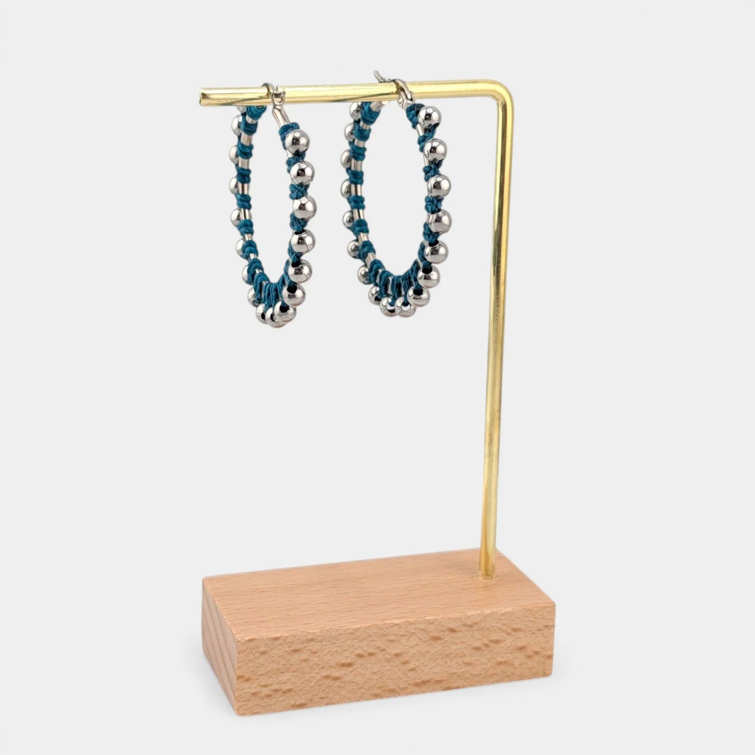 Teal beaded macramé stainless steel hoop earrings in silver, 40 mm drop shown on earring display stand