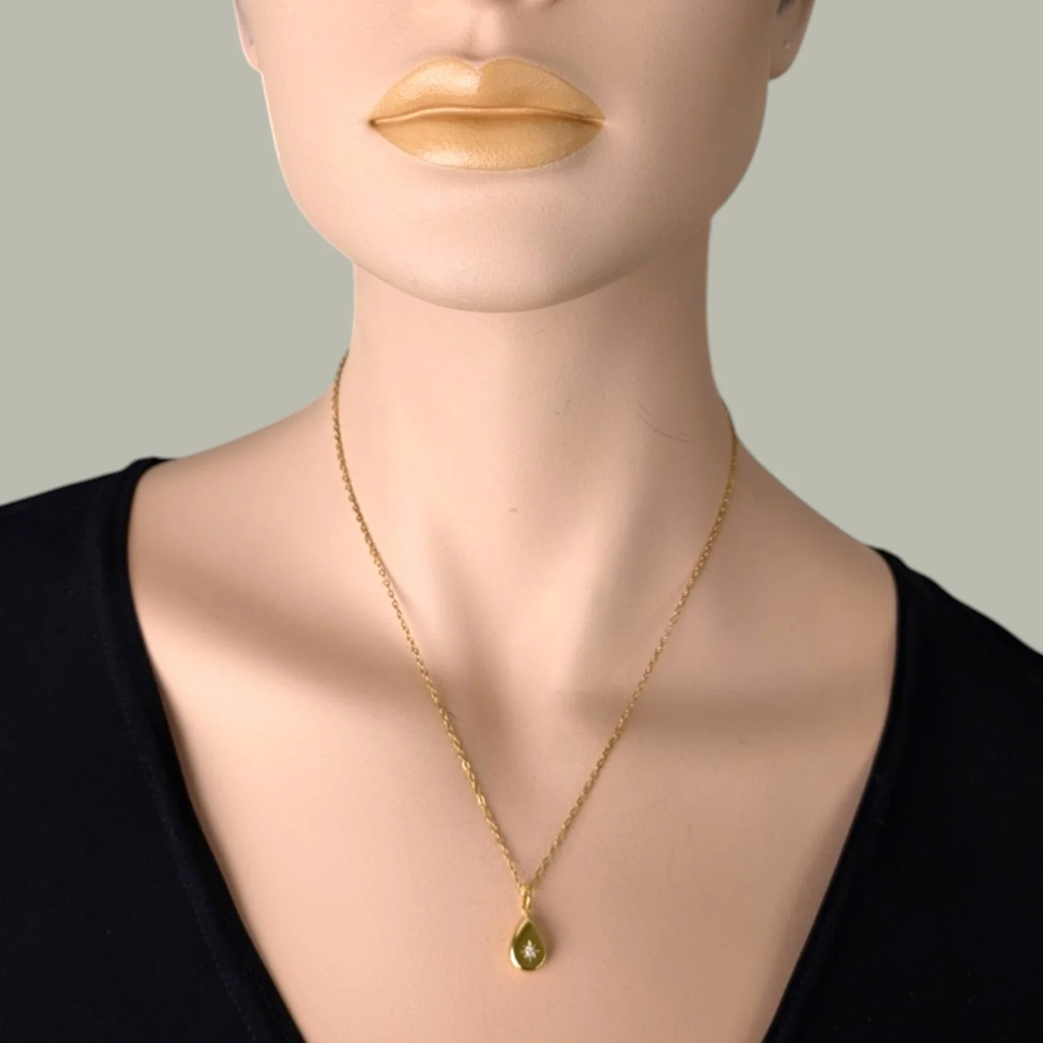 Gold stainless steel starburst teardrop necklace worn on a mannequin, close up bust view