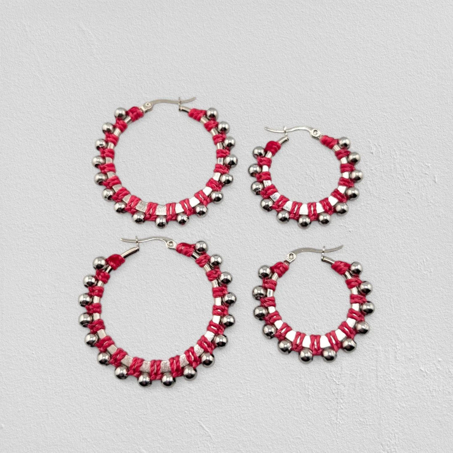 Pink beaded macramé stainless steel hoop earrings in silver, 30 mm and 40 mm sizes side by side, flat lay on a neutral background