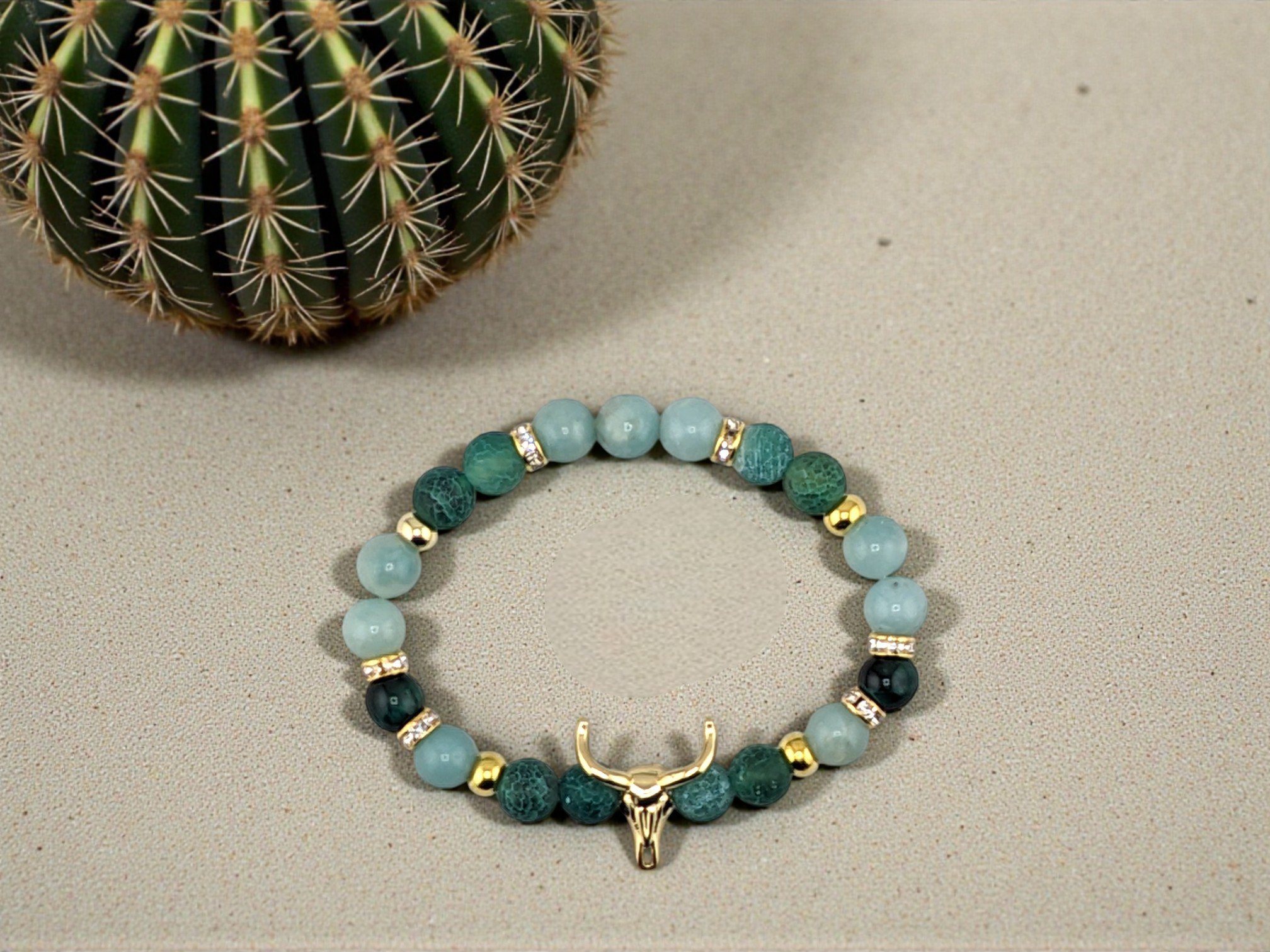 bull skull beaded bracelet with light blue and green gemstones separated by golden spacers and rhinestones, flat lay