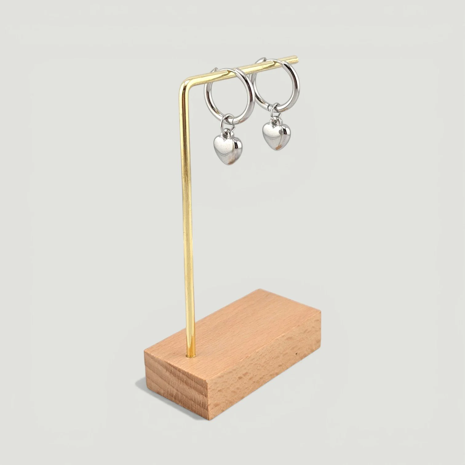 silver puffy heart huggie hoops earrings hanging on a earring stand, showing full drop