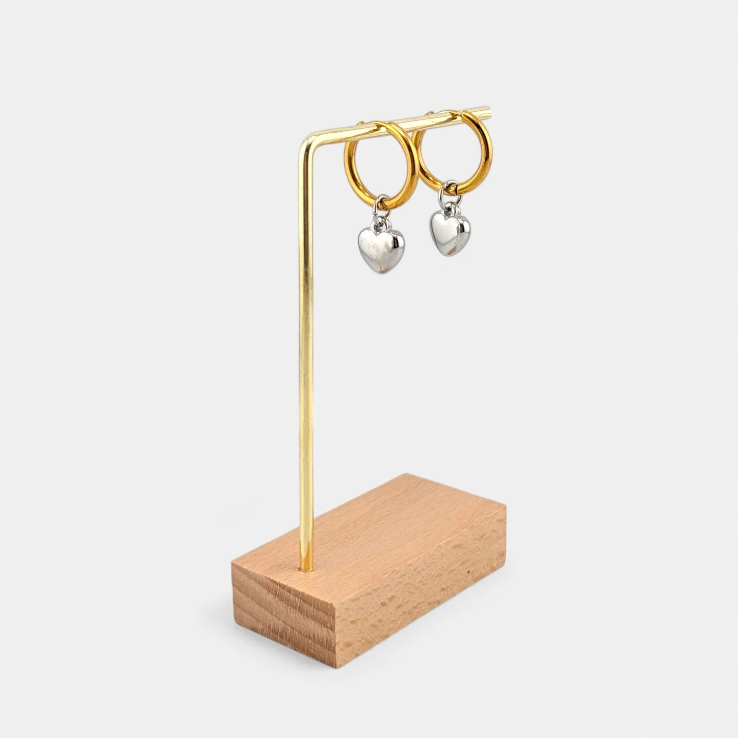 two-tone puffy heart huggie hoop earrings hanging on an earring stand, gold hoops with silver heart charms