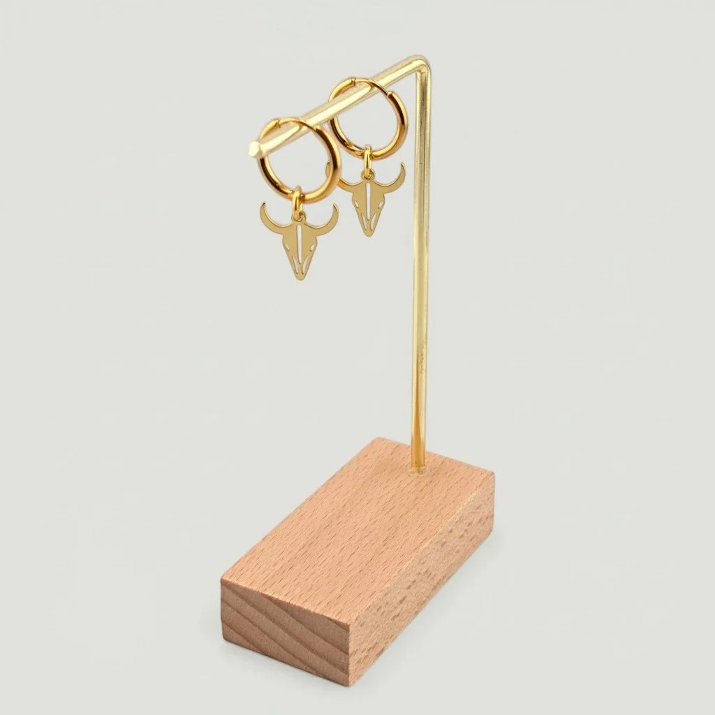 Bull skull stainless steel huggie hoop earrings in gold hanging on display stand, drop view