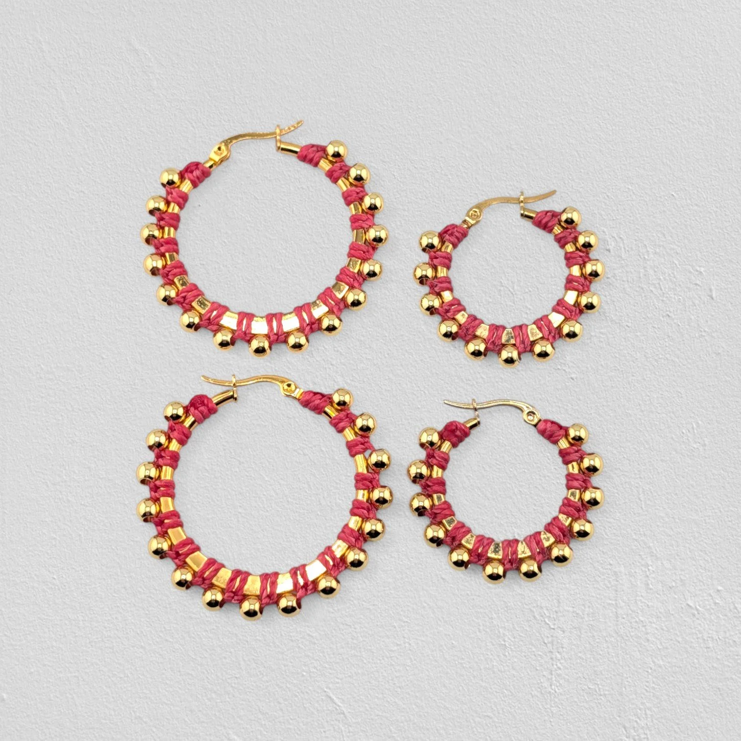 Pink beaded macramé stainless steel hoop earrings in gold, 30 mm and 40 mm sizes side by side, flat lay on a neutral background