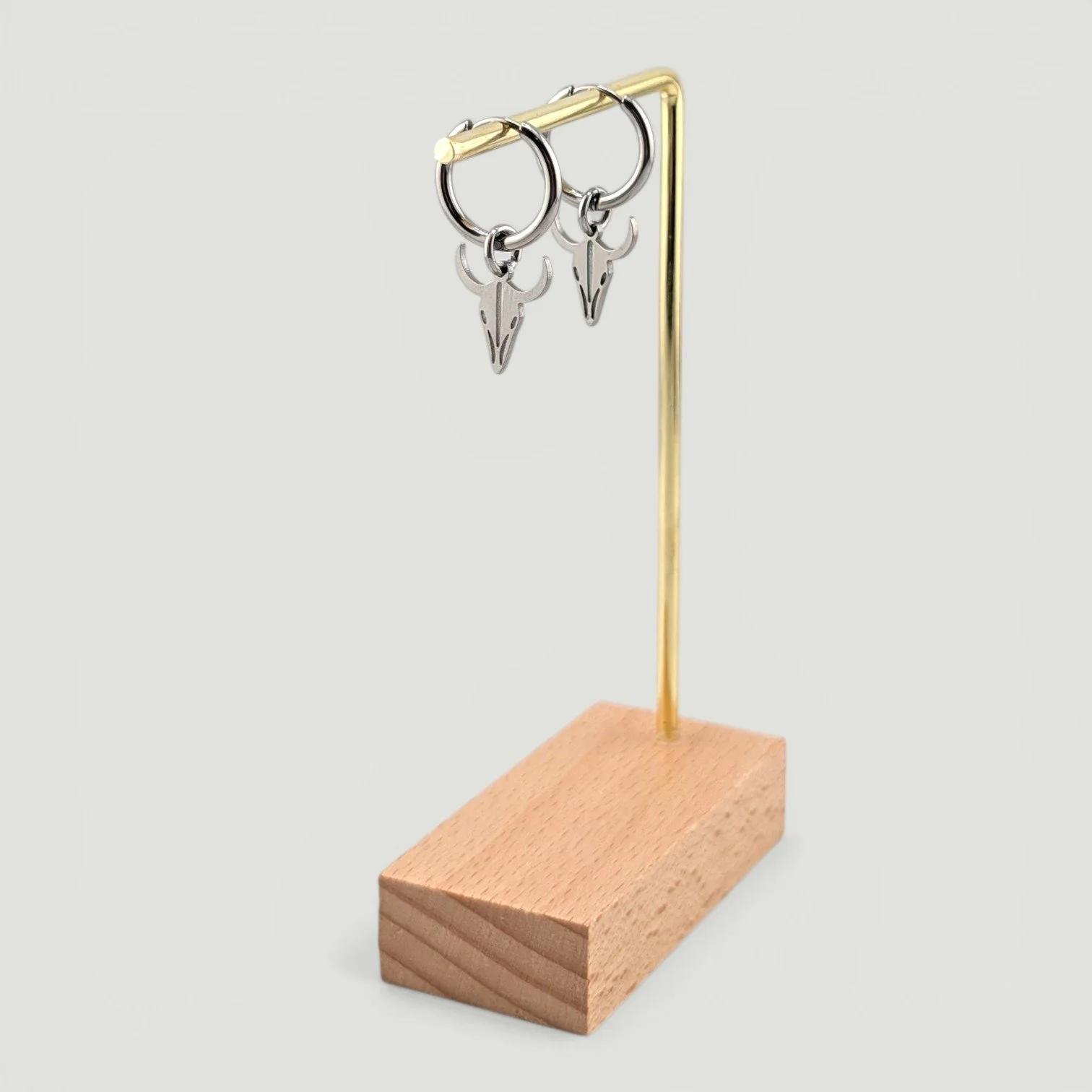 Bull skull stainless steel huggie hoop earrings in silver hanging on display stand, drop view