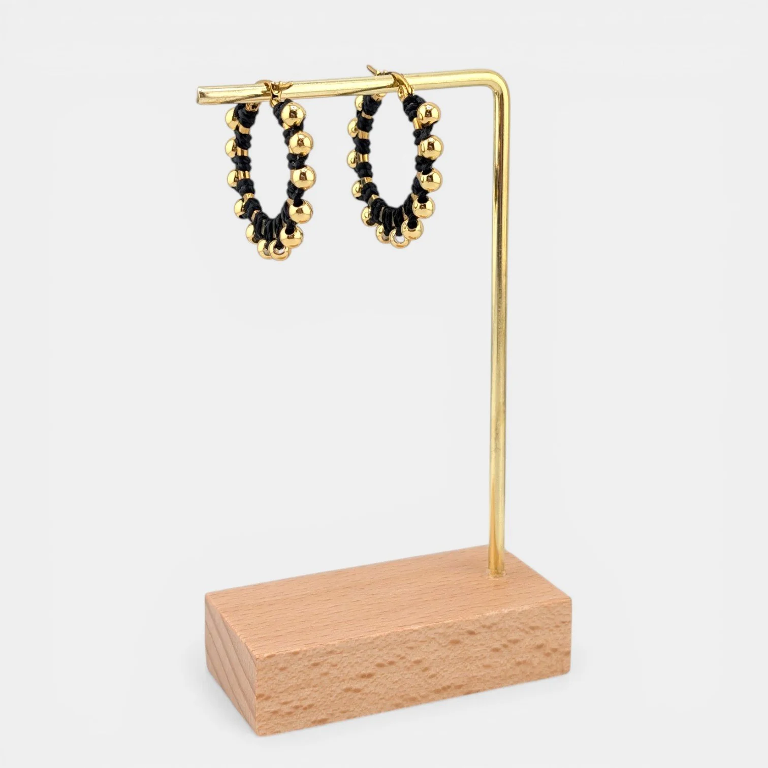 Black beaded macramé stainless steel hoop earrings in gold, 30 mm drop shown on earring display stand