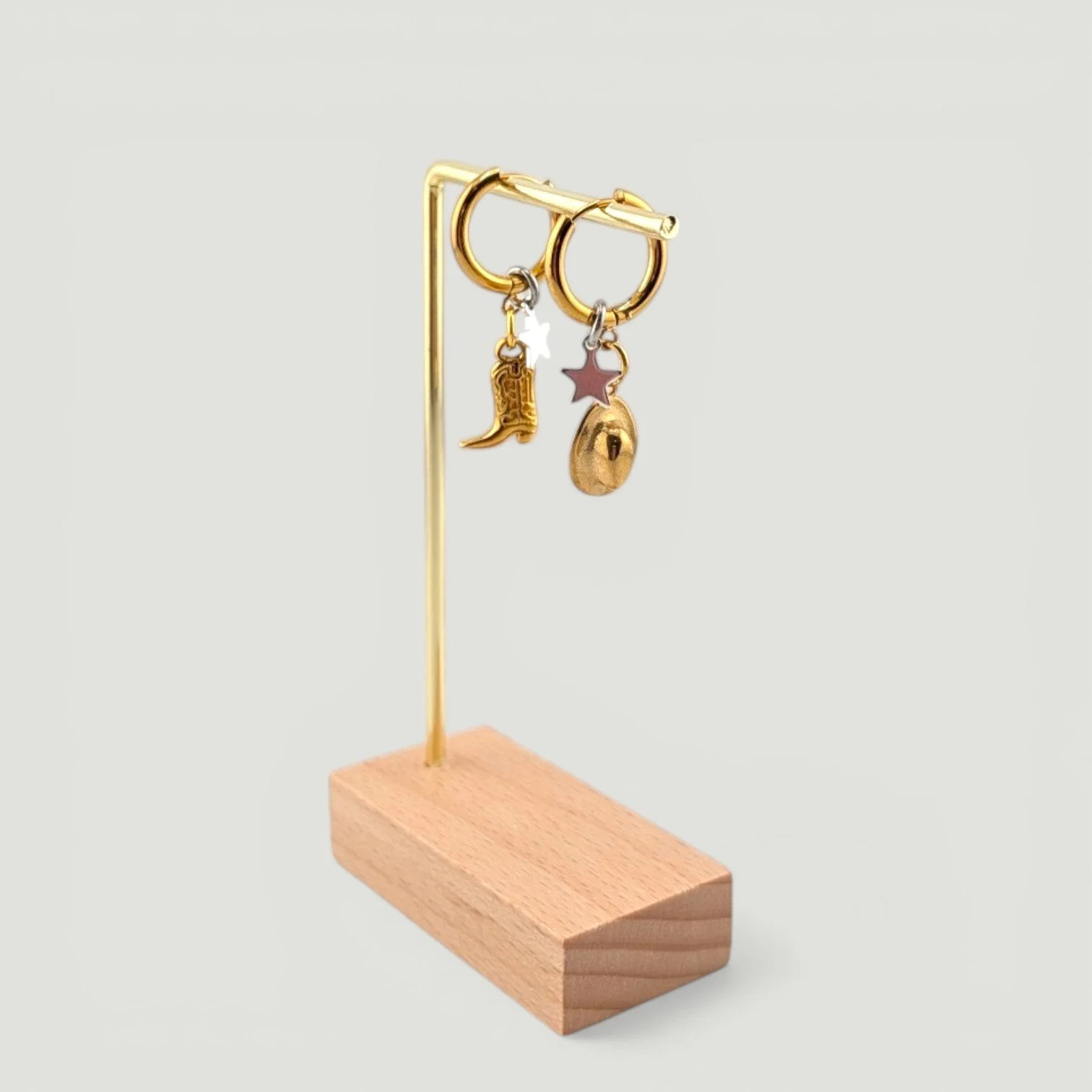 Gold cowboy hat and boot huggie hoop earrings with star charm on display stand, showing drop