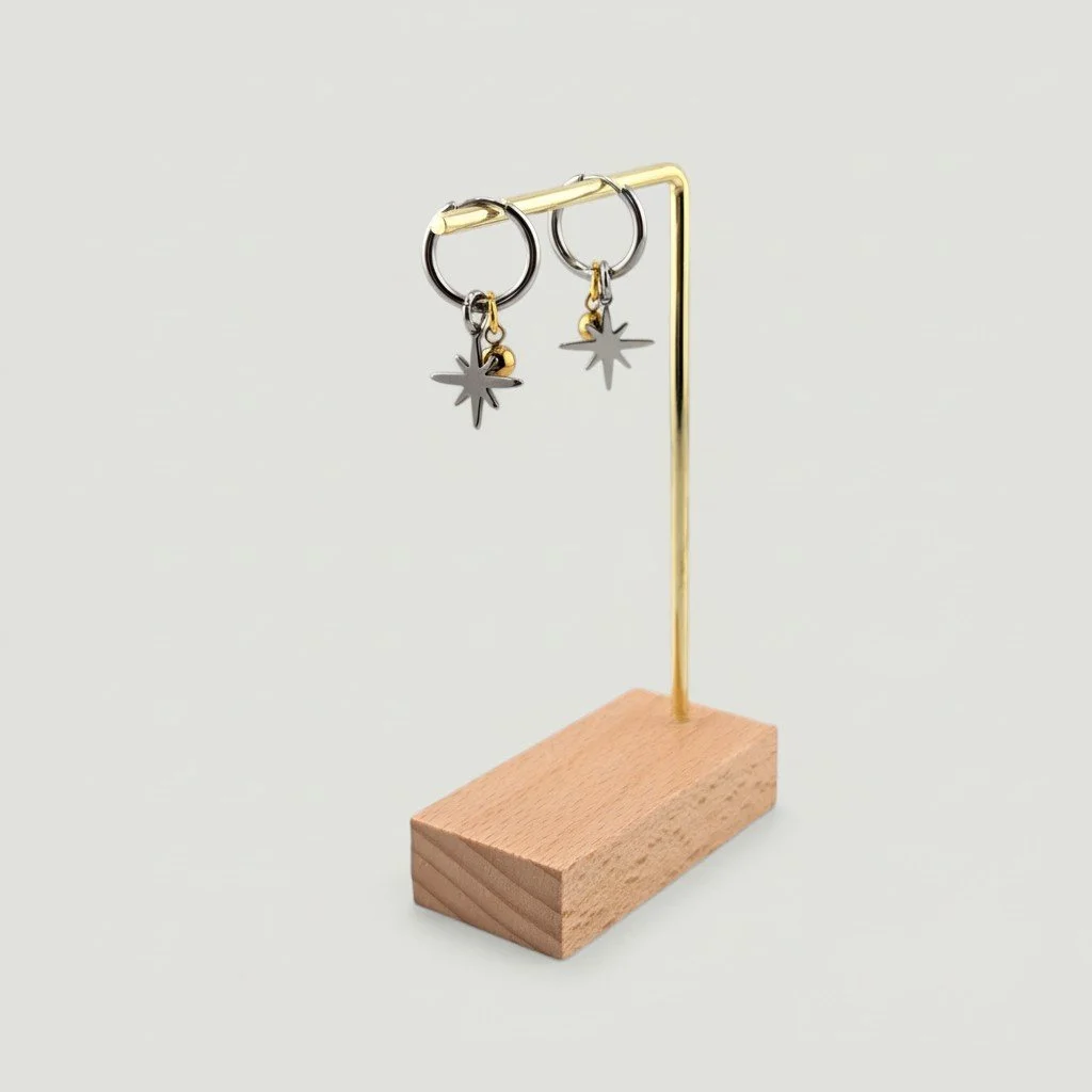 Silver northern star stainless steel huggie hoop earrings with gold bead charm hanging on an earring display stand