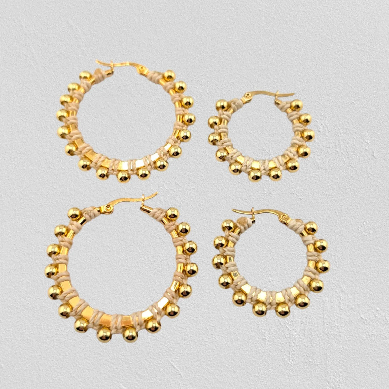 creamy beige beaded macramé stainless steel hoop earrings in gold, 30 mm and 40 mm sizes side by side, flat lay on a neutral background