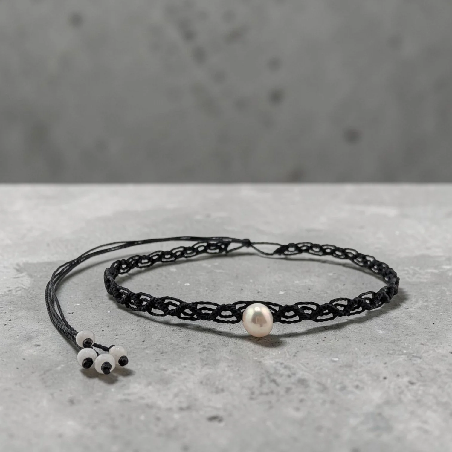 Western macrame woven choker with pearl centerpiece displayed on a textured ciment shelf