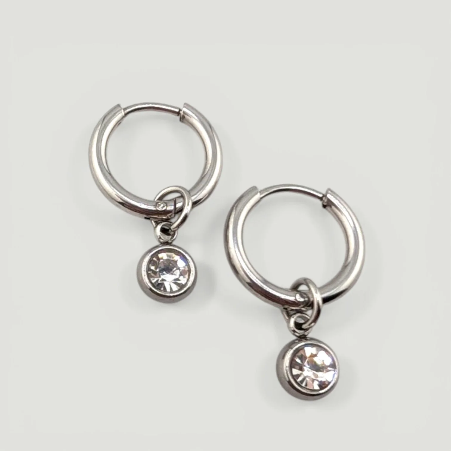 Gold stainless steel huggie hoop earrings with bezel-set rhinestone charms flat lay