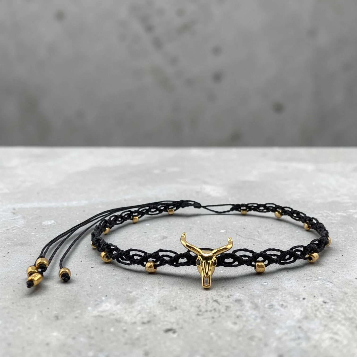 Golden bull skull western woven macrame choker on a textured ciment shelf
