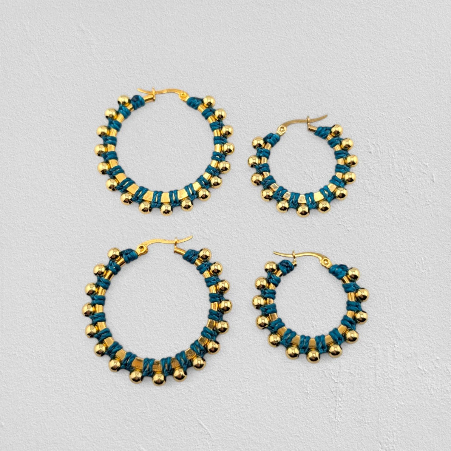 Teal beaded macramé stainless steel hoop earrings in gold, 30 mm and 40 mm sizes side by side, flat lay on a neutral background