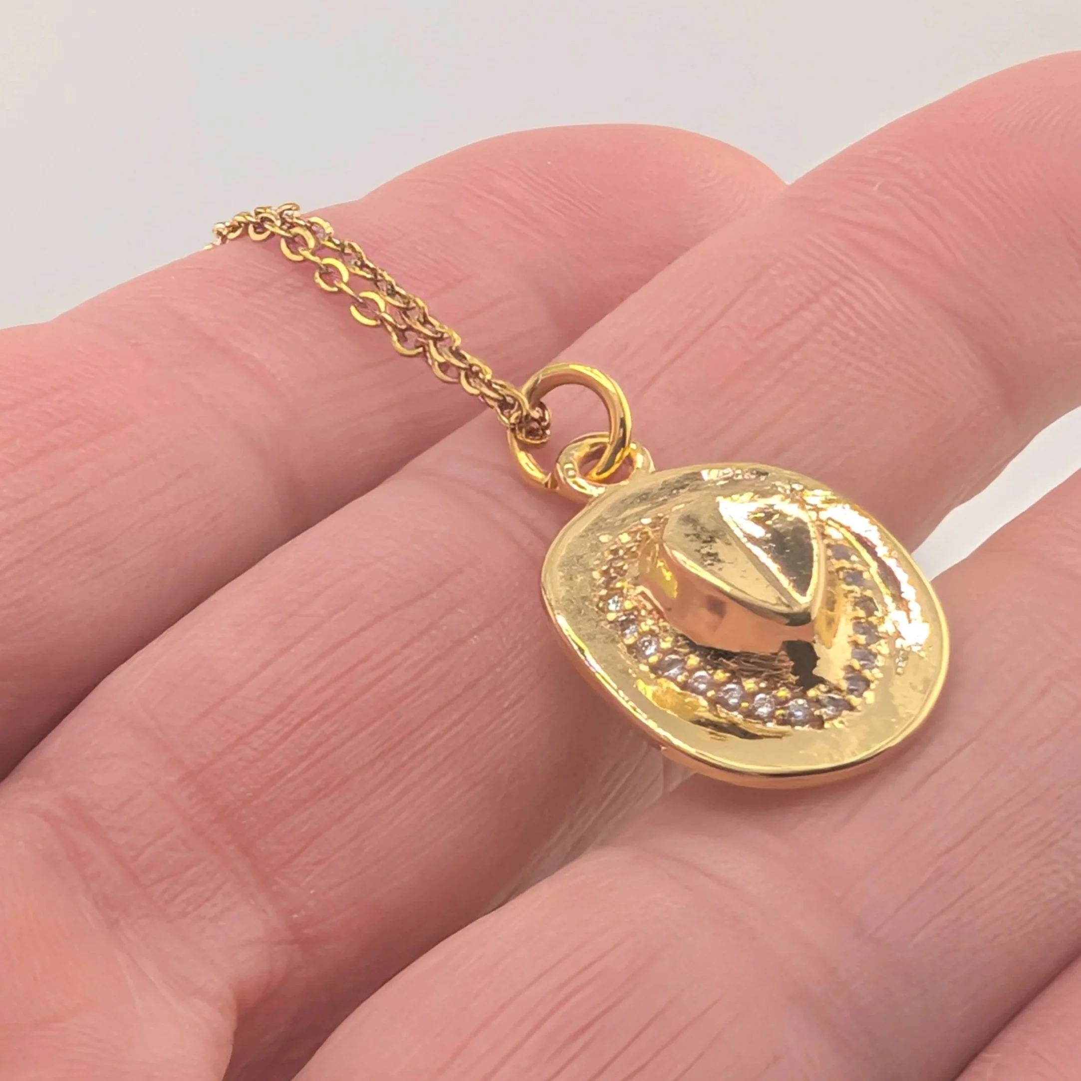 rhinestone cowboy hat necklace on a gold stainless steel chain held in hand, close up detail