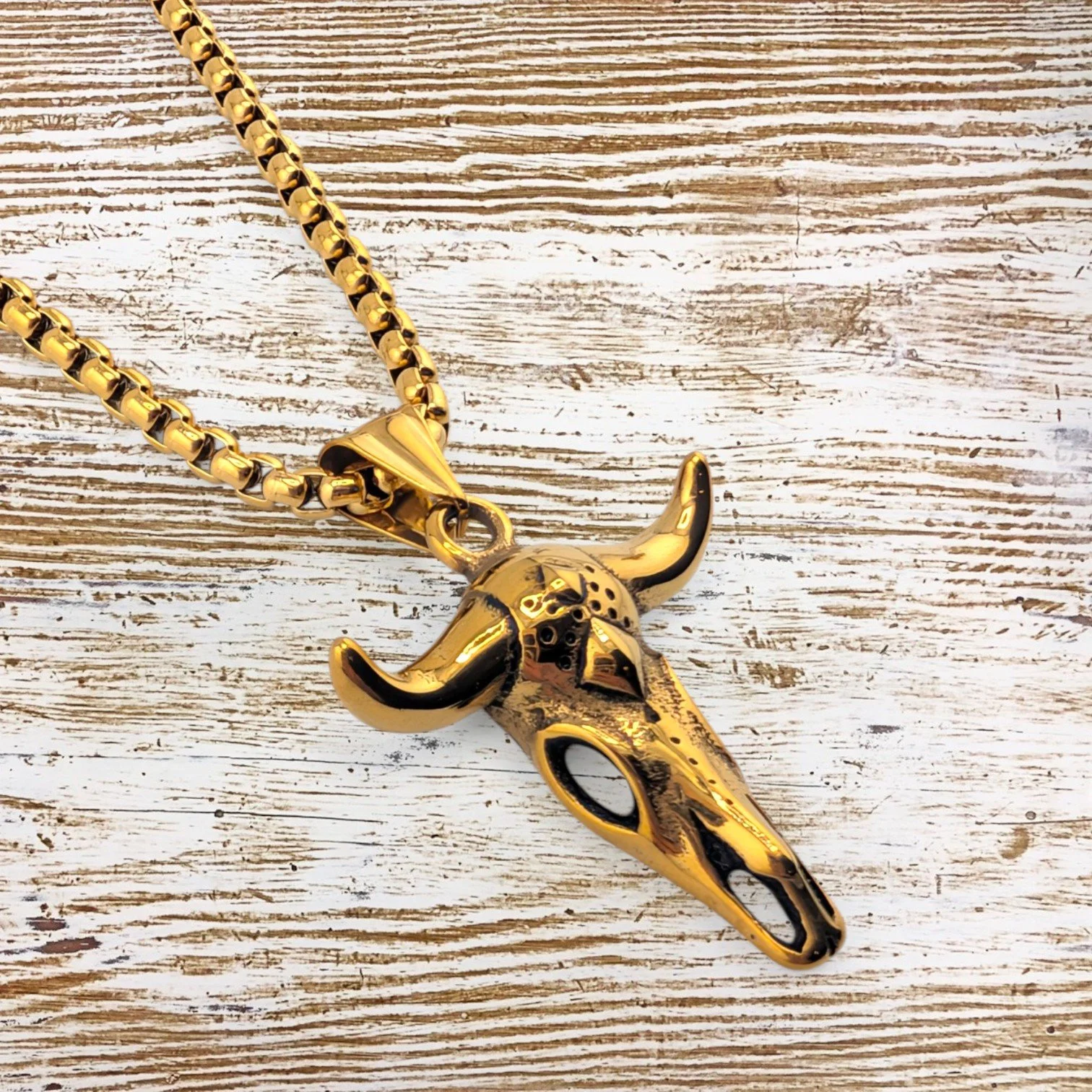 men's bull skull gold stainless steel necklace side view close up showing sculpted pendant detail, on a textured background