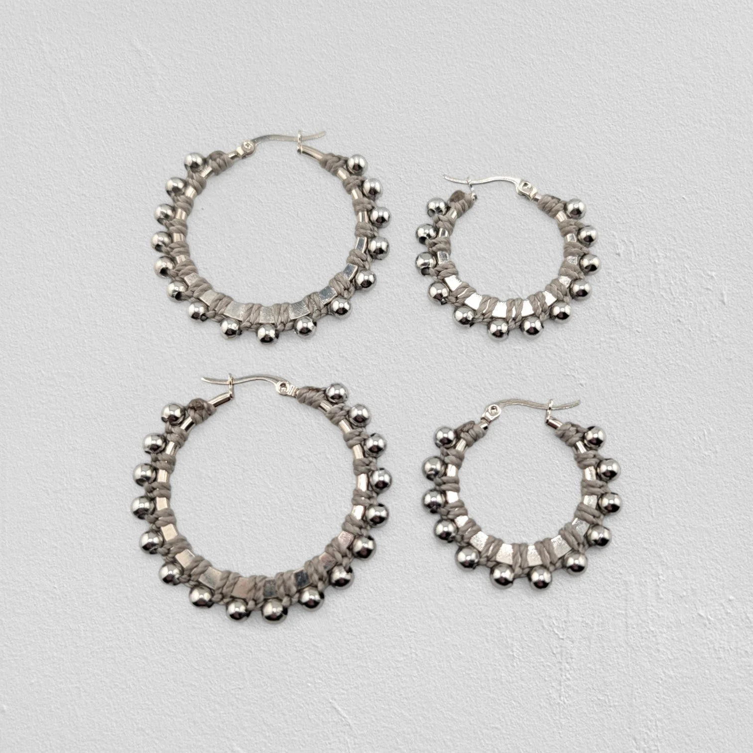 light beaded macramé stainless steel hoop earrings in silver, 30 mm and 40 mm sizes side by side, flat lay on a neutral background
