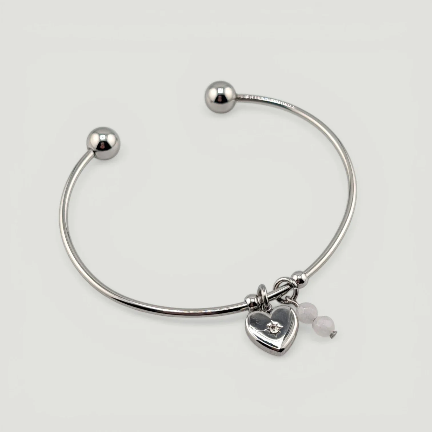 Silver starburst heart stainless steel bangle bracelet with rose quartz charm, full flat lay